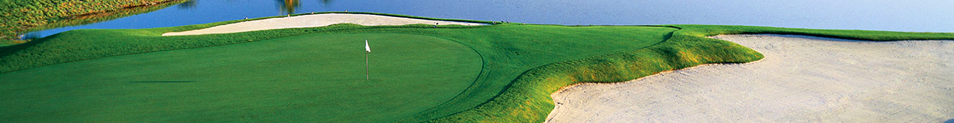 A breathtaking view of a golf course showcasing a green putting area, bordered by a sand trap and a calm waterbody.