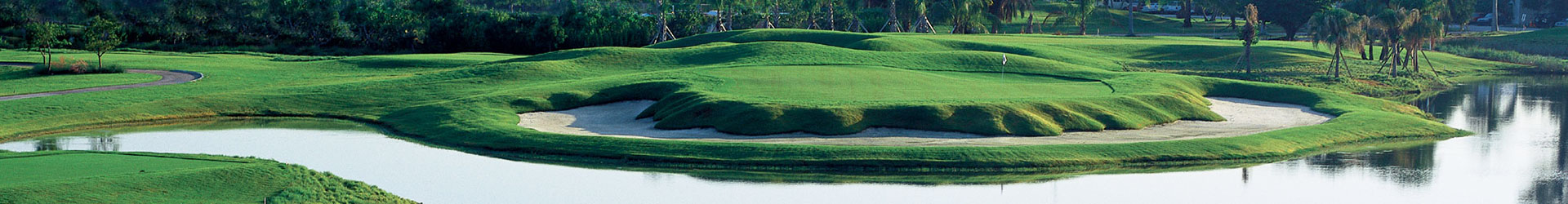 A panoramic view of a stunning golf course featuring lush green hills, a sand trap, and tranquil water edges.